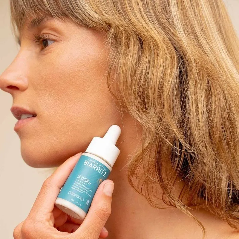 Lifestyle image of a woman applying Laboratoires de Biarritz 1733899 serum to her face, smiling.